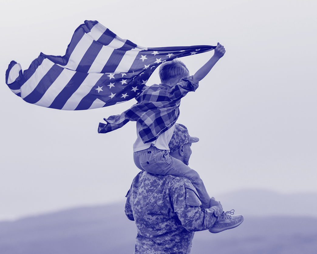child holding American flag sitting on his military father's shoulders